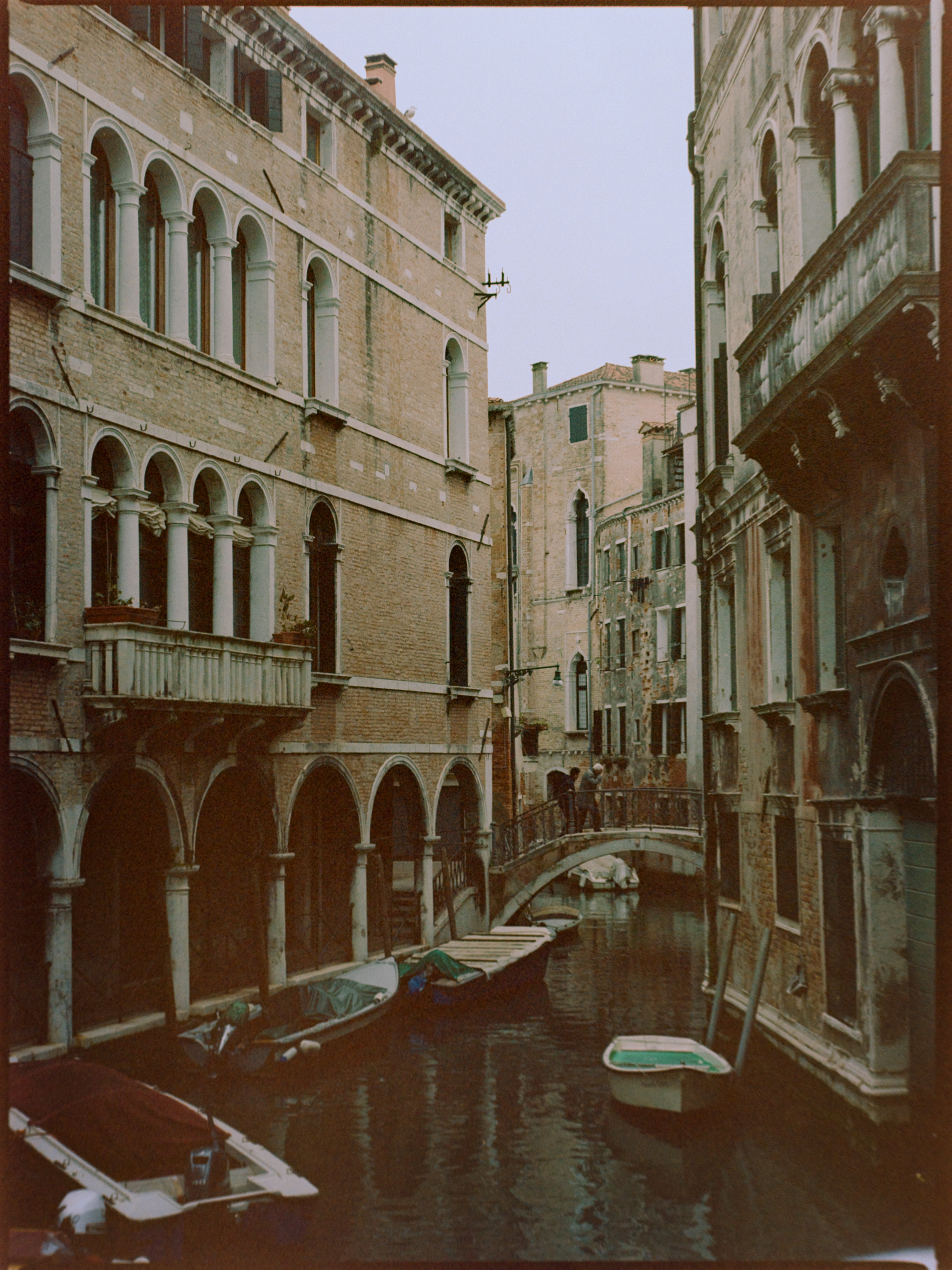 Narrow canal flanked by tall buildings with arched colonnades and moored boats — Venice on film