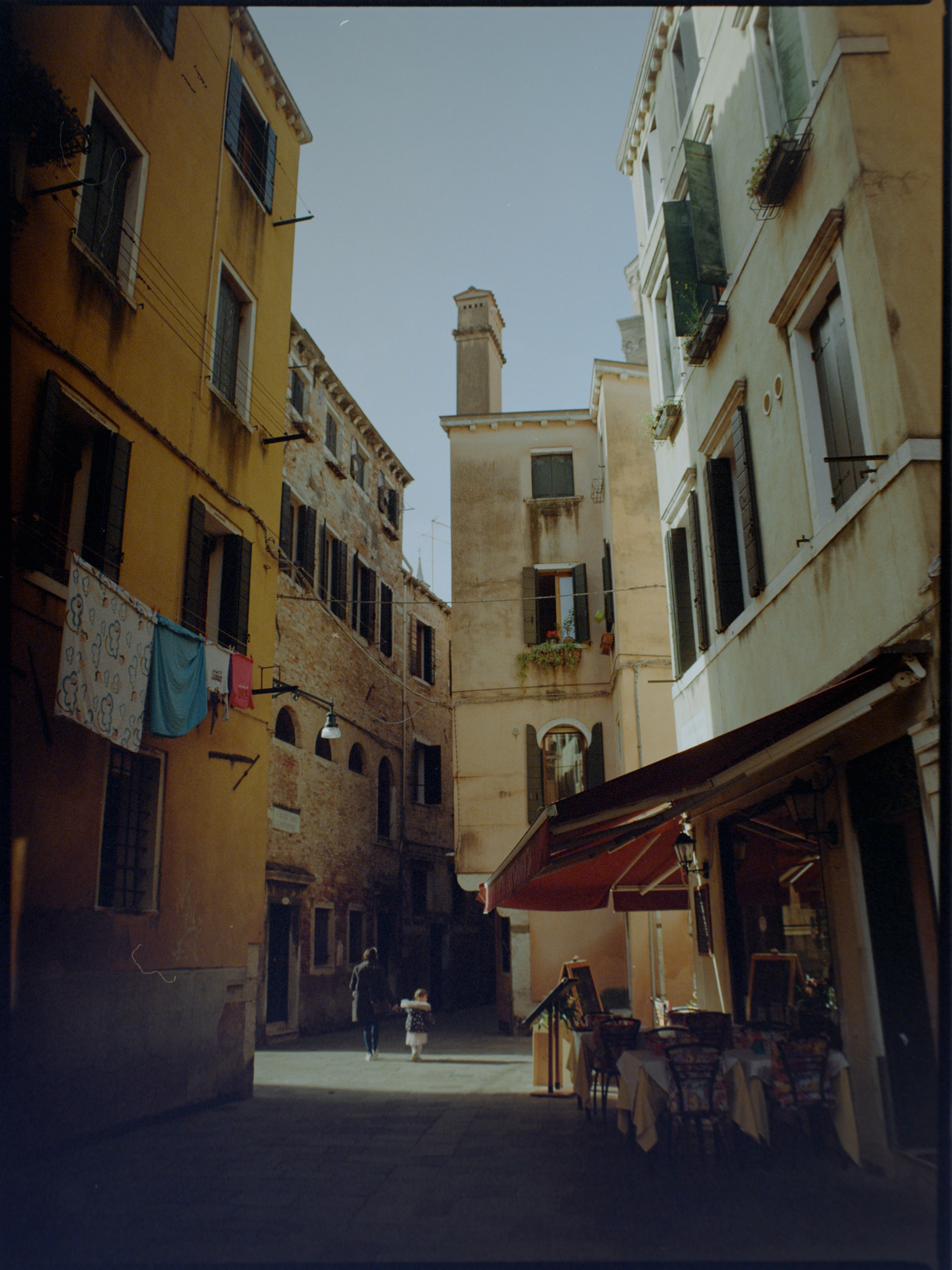 Sun-drenched courtyard with laundry hanging above and restaurant with red awning — Venice street photography