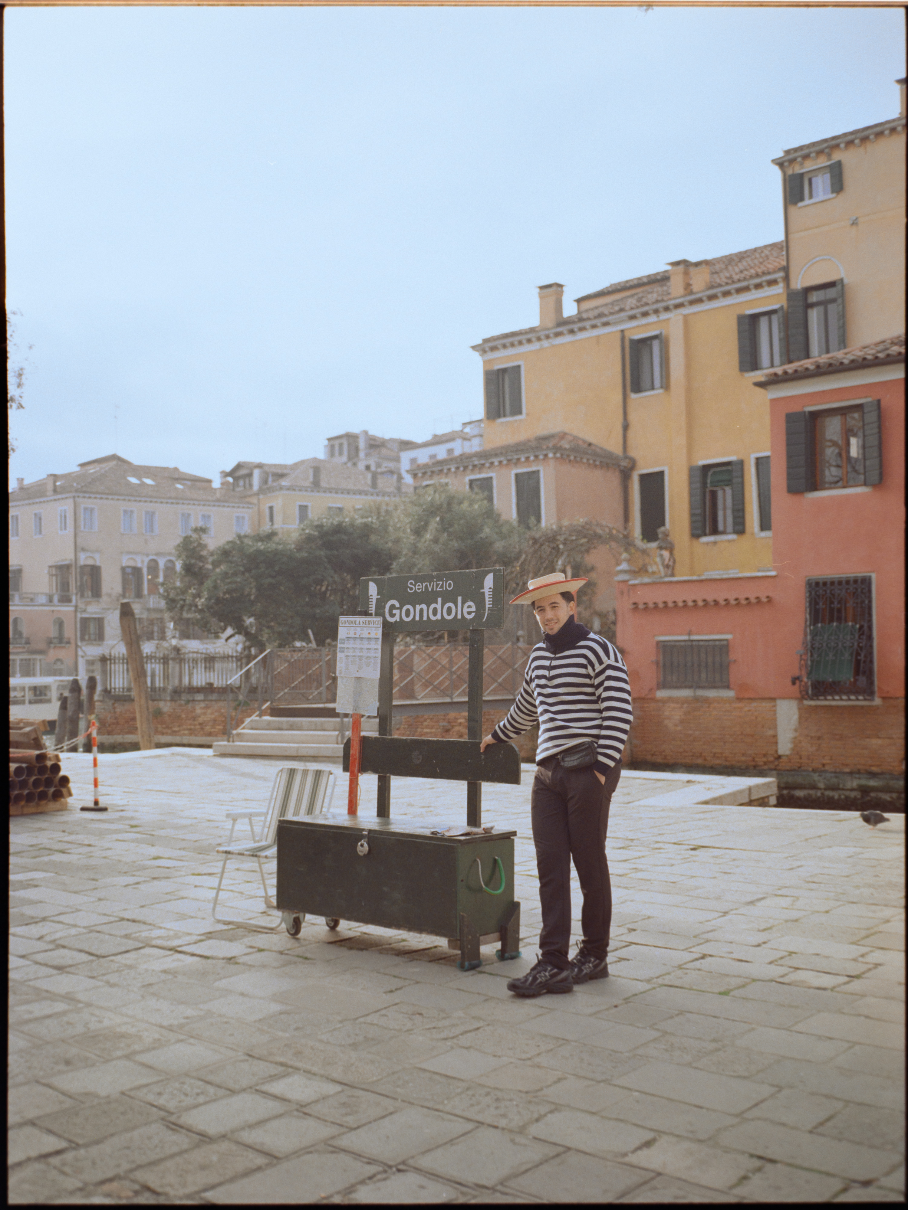 Gondolier standing next to a Servizio Gondole sign in a small campo — Venice portrait on medium format film