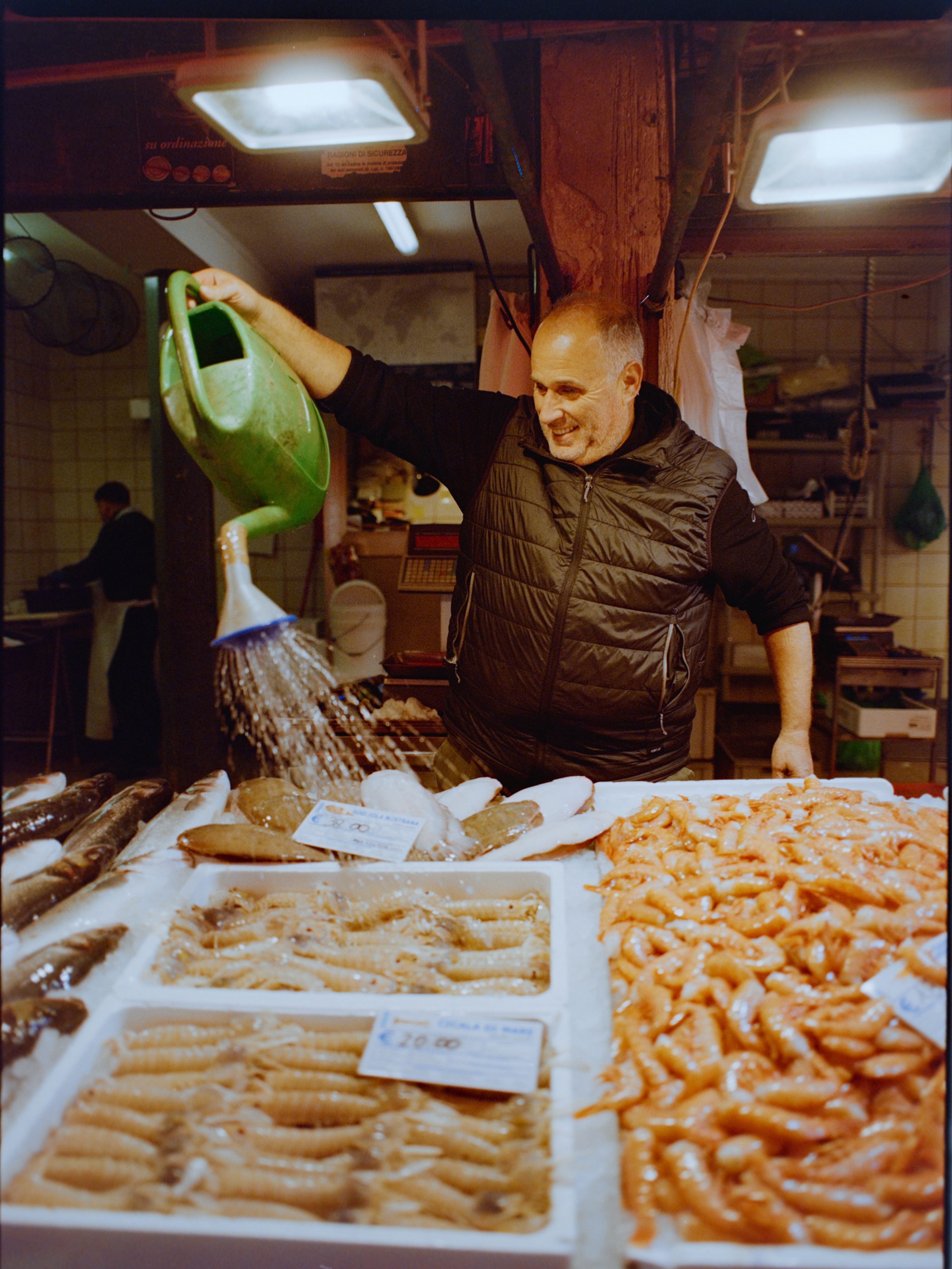 Fish vendor smiling and pouring water over trays of fresh seafood — Venice Rialto Market on medium format film