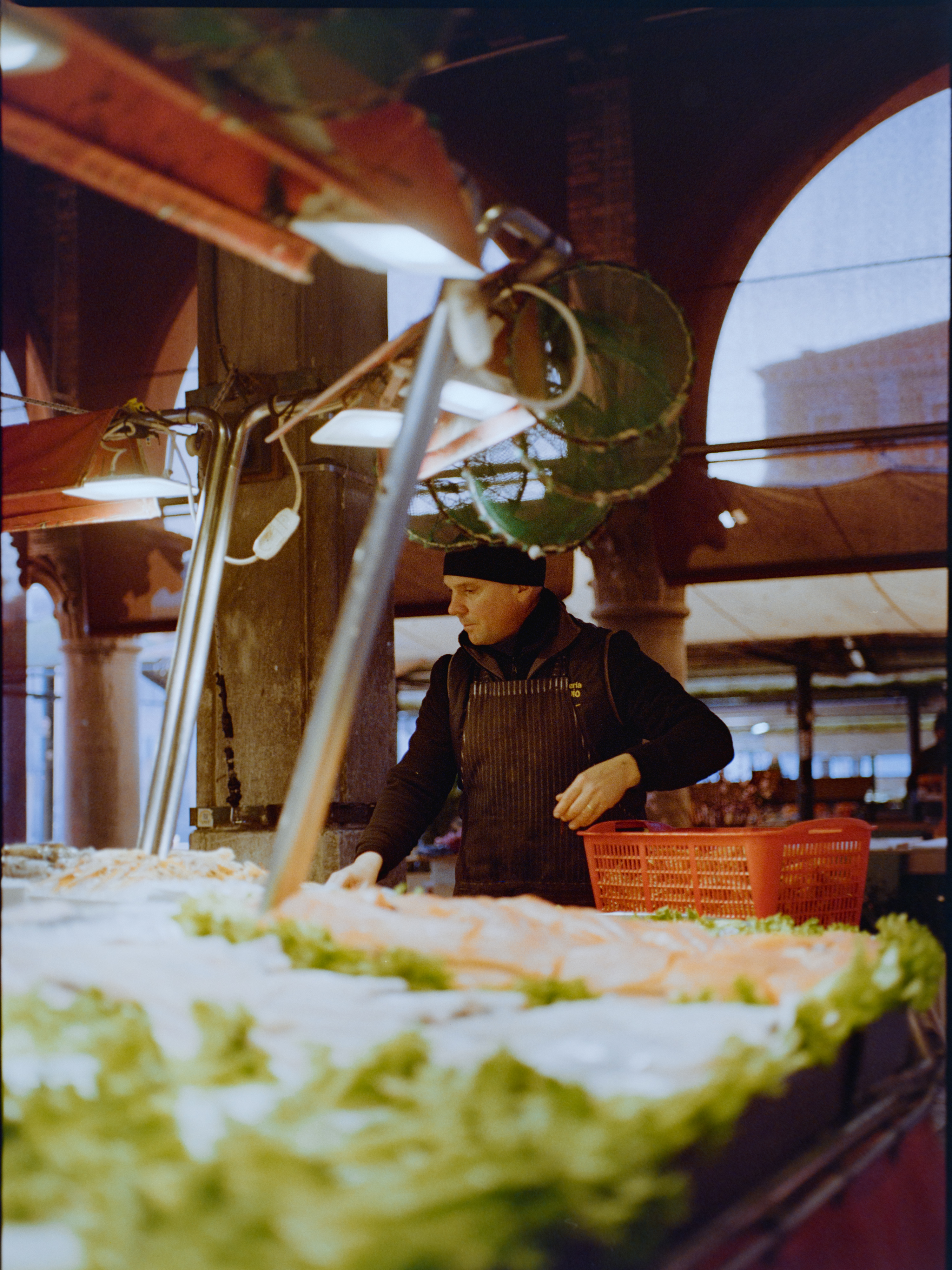 Vendor sorting produce at a market stall under industrial lights — Venice Rialto Market on Kodak Gold 200
