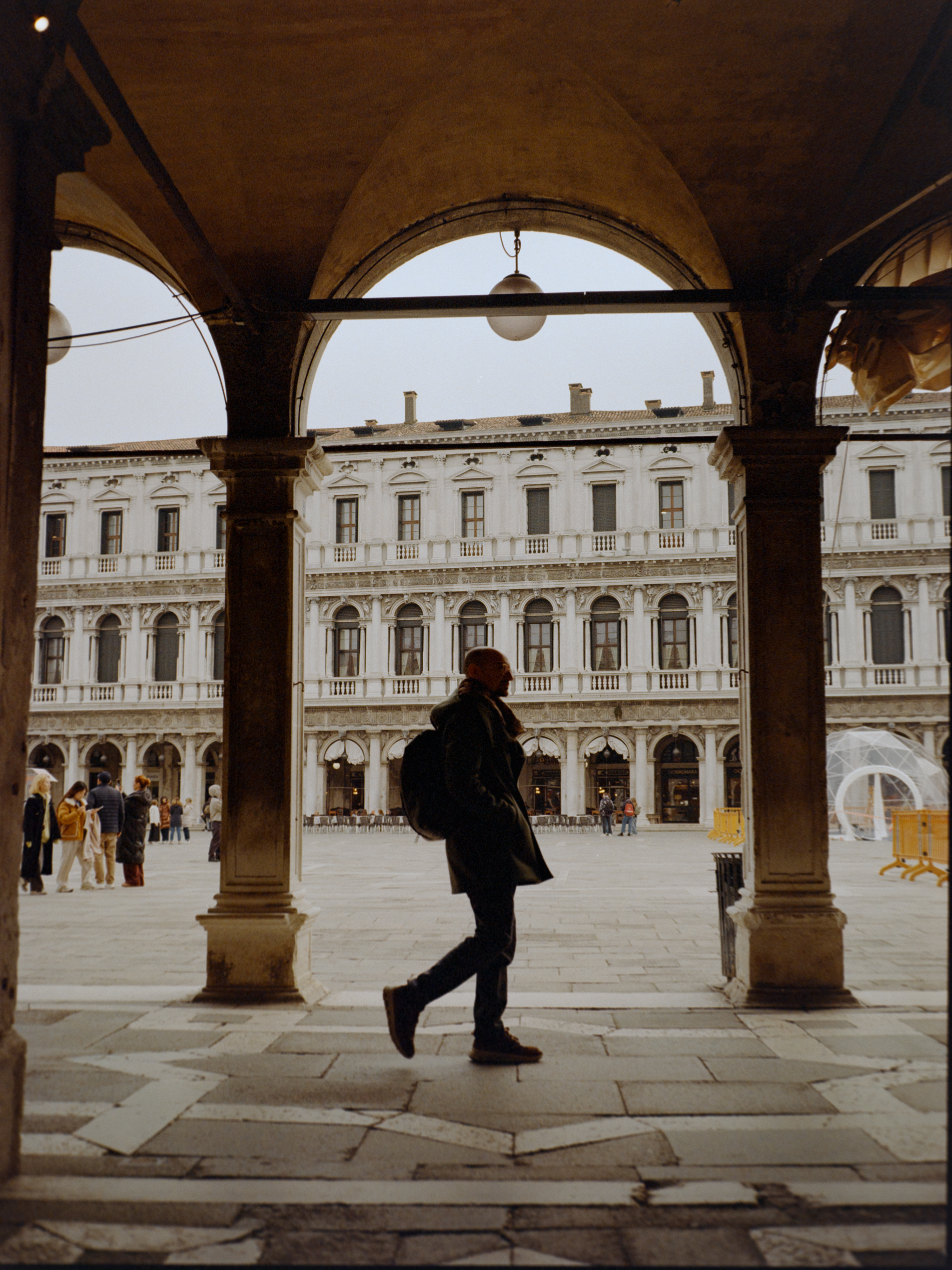 Silhouetted figure walking through the ground-floor arcade with the Procuratie visible behind — Venice on film
